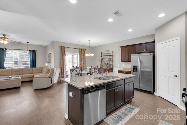 kitchen featuring a center island with sink, sink, light stone countertops, dark brown cabinetry, and stainless steel appliances