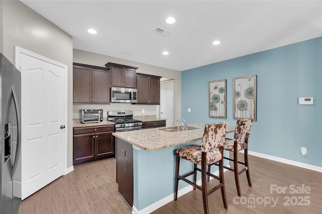 kitchen featuring a kitchen island with sink, sink, light hardwood / wood-style flooring, appliances with stainless steel finishes, and dark brown cabinetry