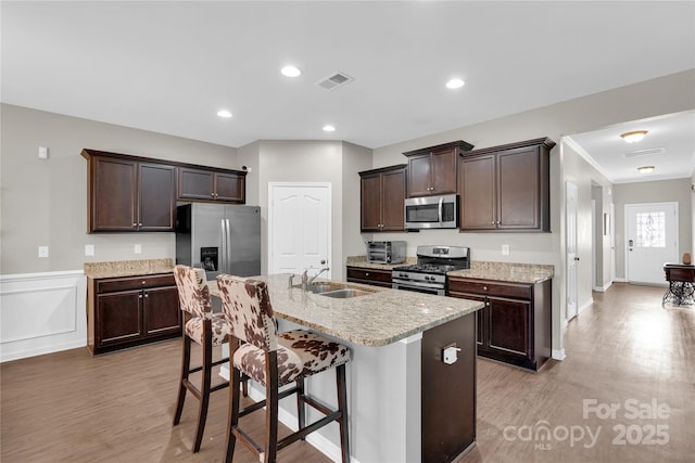 kitchen with sink, stainless steel appliances, a kitchen breakfast bar, a kitchen island with sink, and dark brown cabinets