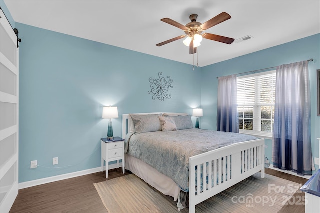 bedroom featuring ceiling fan, a barn door, and dark hardwood / wood-style floors