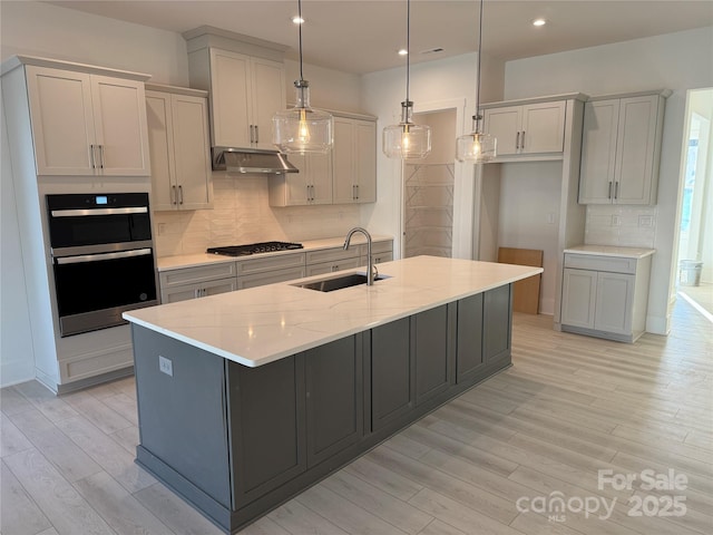 kitchen featuring pendant lighting, a center island with sink, sink, light stone countertops, and appliances with stainless steel finishes