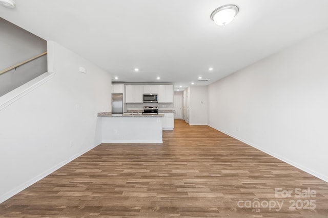 kitchen with light stone counters, light hardwood / wood-style flooring, kitchen peninsula, white cabinets, and appliances with stainless steel finishes