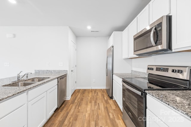 kitchen with light stone counters, stainless steel appliances, white cabinetry, and sink