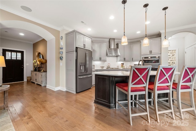 kitchen featuring hanging light fixtures, stainless steel appliances, wall chimney range hood, backsplash, and gray cabinets