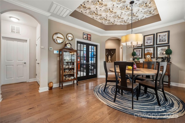 dining room featuring french doors, ornamental molding, a tray ceiling, an inviting chandelier, and hardwood / wood-style floors