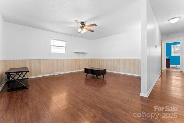 living area with ceiling fan, a textured ceiling, and dark hardwood / wood-style floors