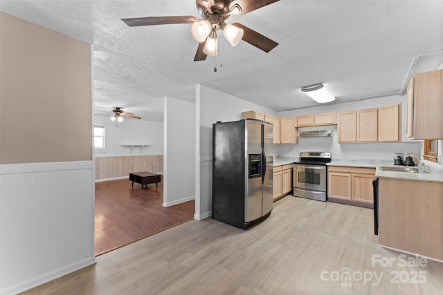 kitchen with light brown cabinets, stainless steel appliances, light hardwood / wood-style floors, sink, and wood walls