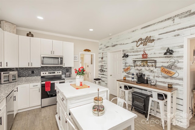 kitchen with appliances with stainless steel finishes, a kitchen island, white cabinetry, decorative backsplash, and light wood-type flooring