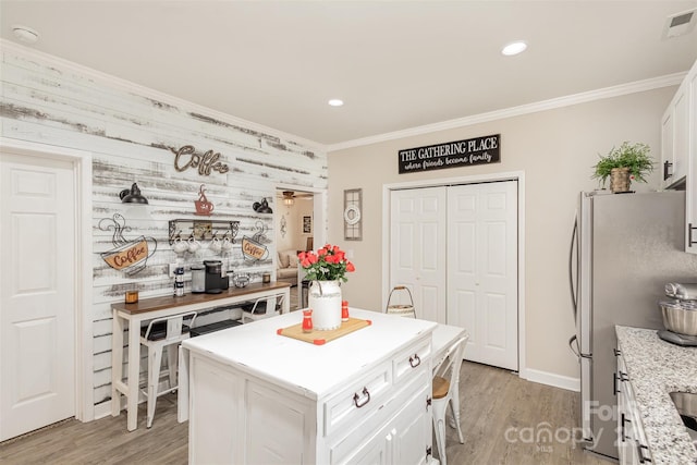 kitchen featuring white cabinets, a center island, wood walls, stainless steel refrigerator, and light hardwood / wood-style flooring