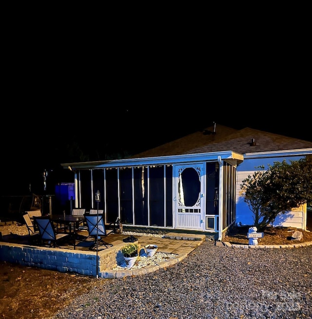 back house at night featuring a patio and a sunroom