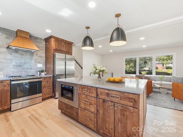 kitchen featuring pendant lighting, a center island, wall chimney exhaust hood, appliances with stainless steel finishes, and light hardwood / wood-style floors