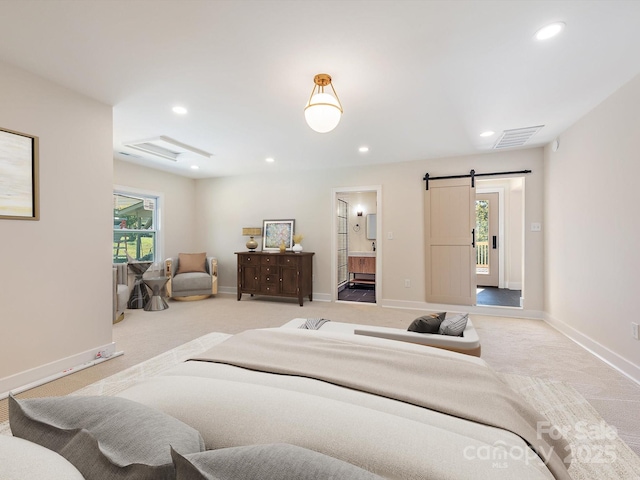 bedroom with ensuite bathroom, a barn door, and light carpet