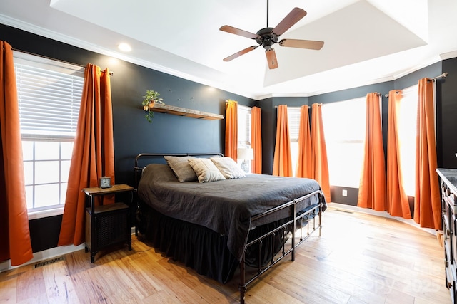 bedroom featuring ceiling fan, a raised ceiling, and light wood-type flooring