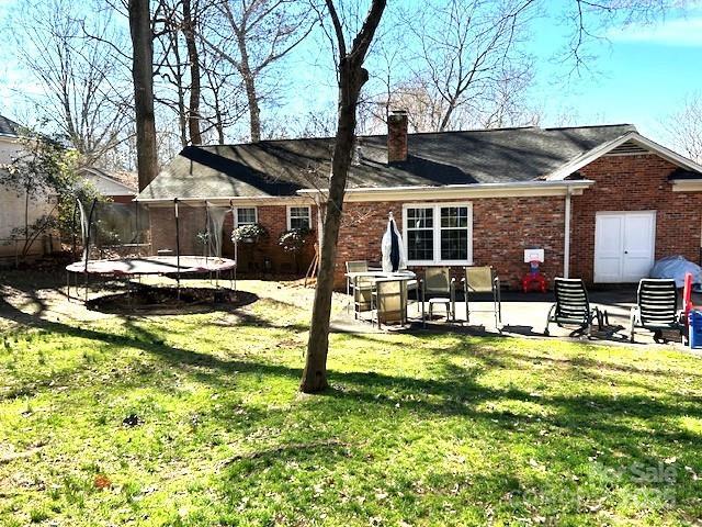 back of property featuring a patio area, a trampoline, and a lawn