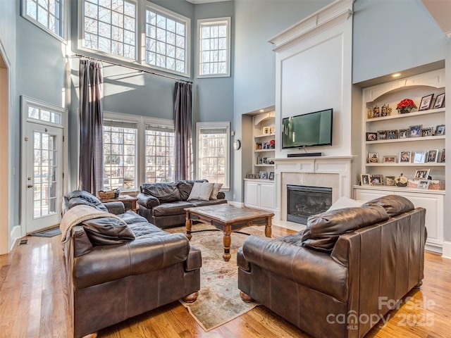 living room featuring light hardwood / wood-style floors, a healthy amount of sunlight, a towering ceiling, and built in shelves