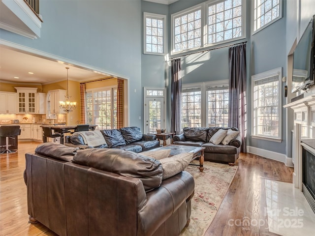 living room featuring light hardwood / wood-style floors, a premium fireplace, a towering ceiling, crown molding, and a notable chandelier