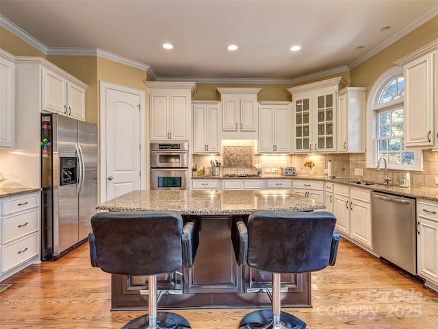 kitchen featuring a kitchen breakfast bar, appliances with stainless steel finishes, crown molding, light stone counters, and a kitchen island