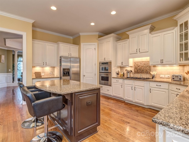 kitchen with appliances with stainless steel finishes, white cabinetry, light stone counters, and a kitchen island