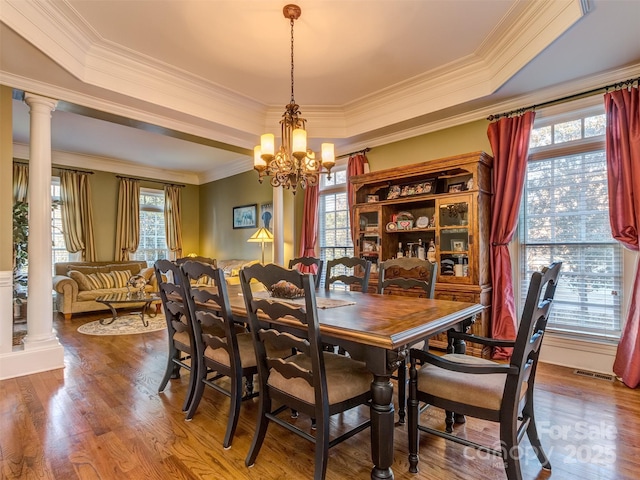 dining room featuring a raised ceiling, crown molding, a chandelier, and ornate columns