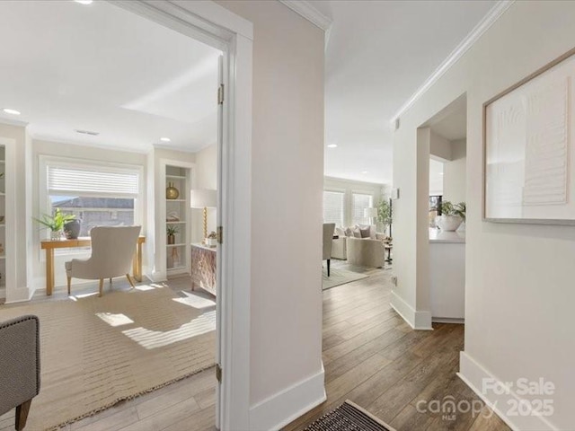 hallway featuring built in shelves, crown molding, hardwood / wood-style floors, and a wealth of natural light