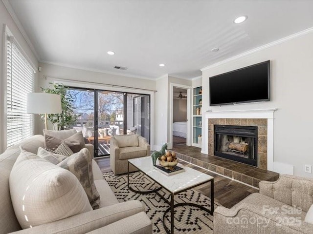 living room with a tiled fireplace, hardwood / wood-style floors, crown molding, and built in shelves