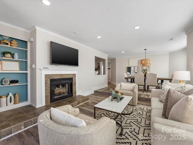 living room featuring built in shelves, dark hardwood / wood-style floors, ornamental molding, and a tile fireplace