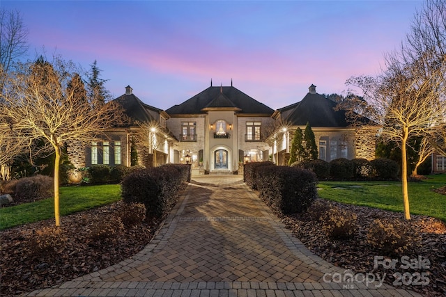 view of front facade featuring decorative driveway, stone siding, a front lawn, and stucco siding