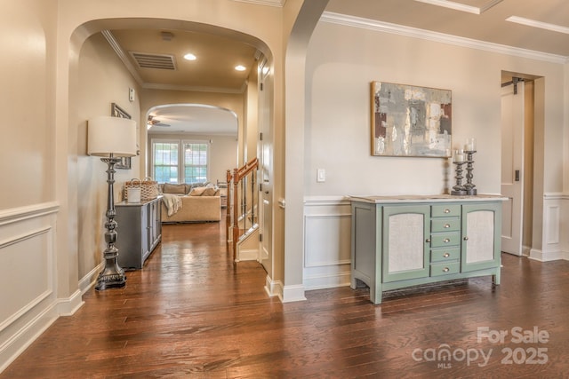 hallway featuring dark wood-style floors, visible vents, a decorative wall, and crown molding