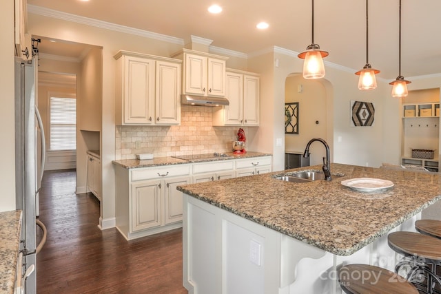 kitchen featuring under cabinet range hood, dark wood-type flooring, a sink, a kitchen breakfast bar, and freestanding refrigerator