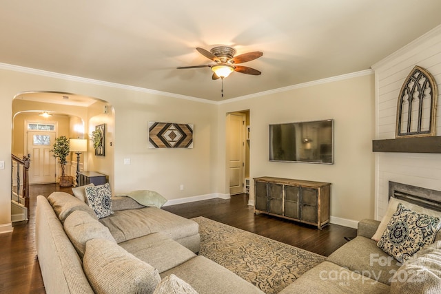 living area with arched walkways, a fireplace, ornamental molding, wood finished floors, and baseboards