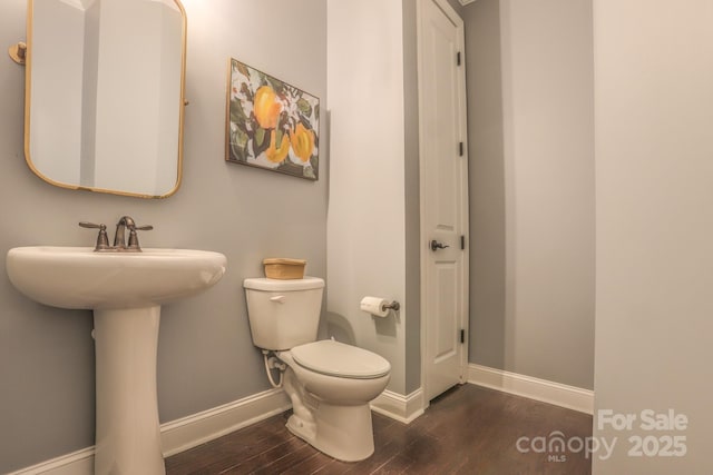 half bathroom with toilet, a sink, baseboards, and wood finished floors