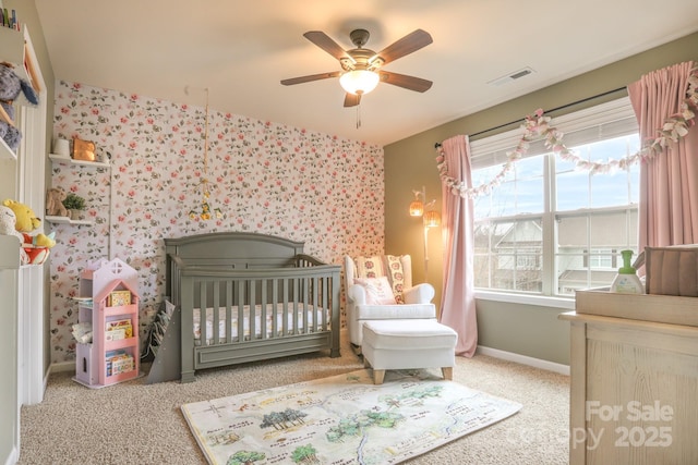 carpeted bedroom with a ceiling fan, visible vents, a crib, and baseboards