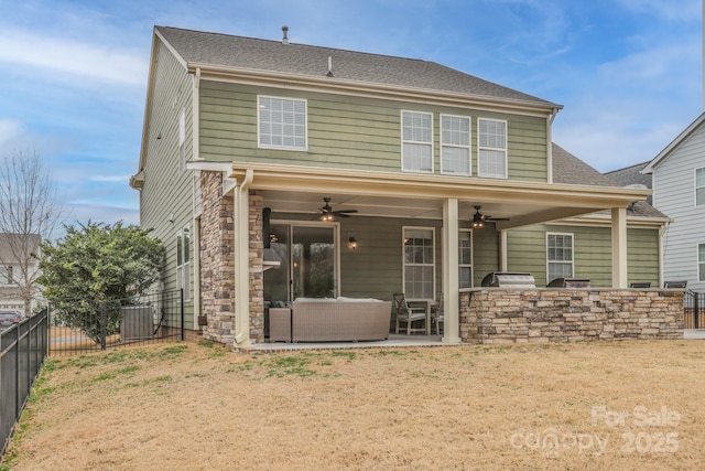 rear view of property featuring stone siding, a fenced backyard, an outdoor kitchen, and a patio