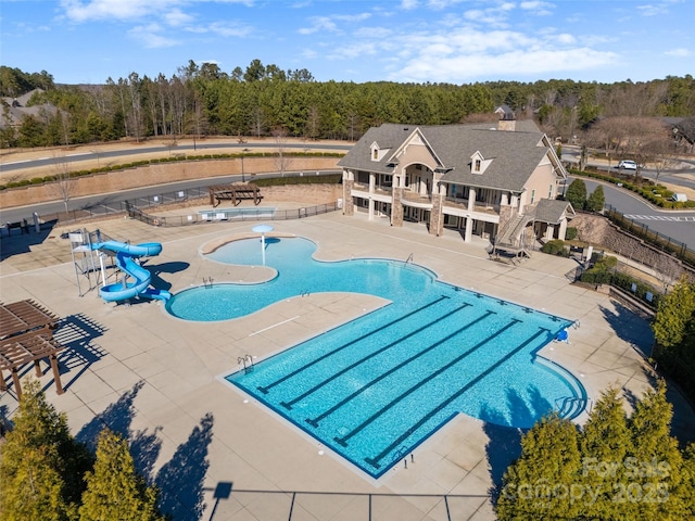 pool with a water slide, fence, and a patio