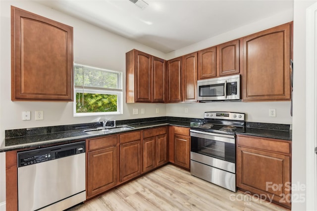 kitchen featuring dark stone countertops, sink, light wood-type flooring, and stainless steel appliances