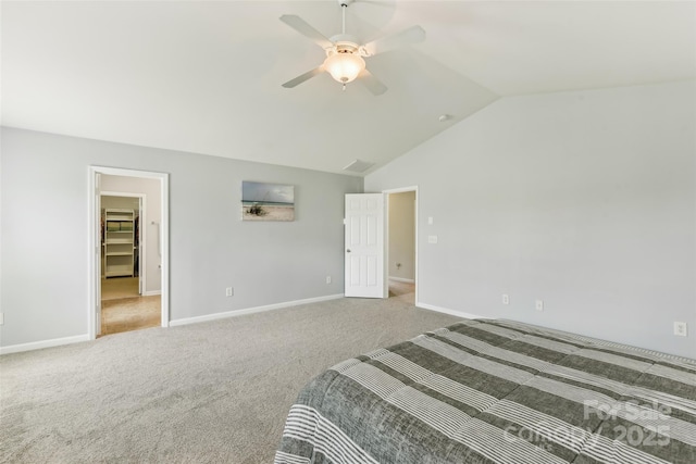 carpeted bedroom with a walk in closet, vaulted ceiling, and ceiling fan