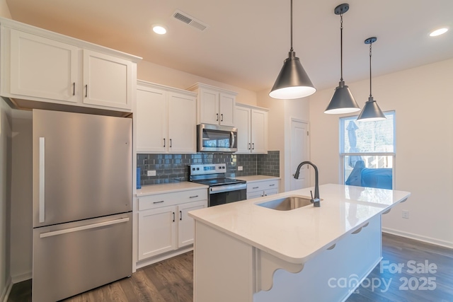 kitchen featuring stainless steel appliances, a sink, visible vents, backsplash, and a center island with sink