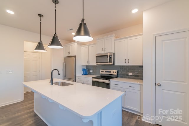 kitchen with a kitchen island with sink, stainless steel appliances, a sink, white cabinetry, and tasteful backsplash