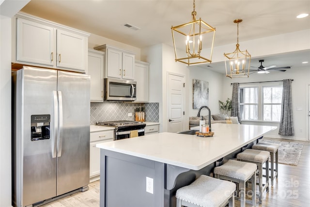 kitchen with a kitchen island with sink, white cabinets, hanging light fixtures, ceiling fan, and stainless steel appliances