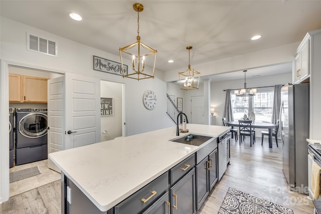 kitchen featuring appliances with stainless steel finishes, sink, pendant lighting, light hardwood / wood-style flooring, and an island with sink