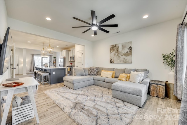 living room with ceiling fan with notable chandelier, light hardwood / wood-style flooring, and sink