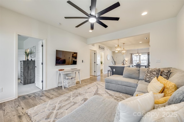 living room featuring light hardwood / wood-style flooring, ceiling fan with notable chandelier, and sink