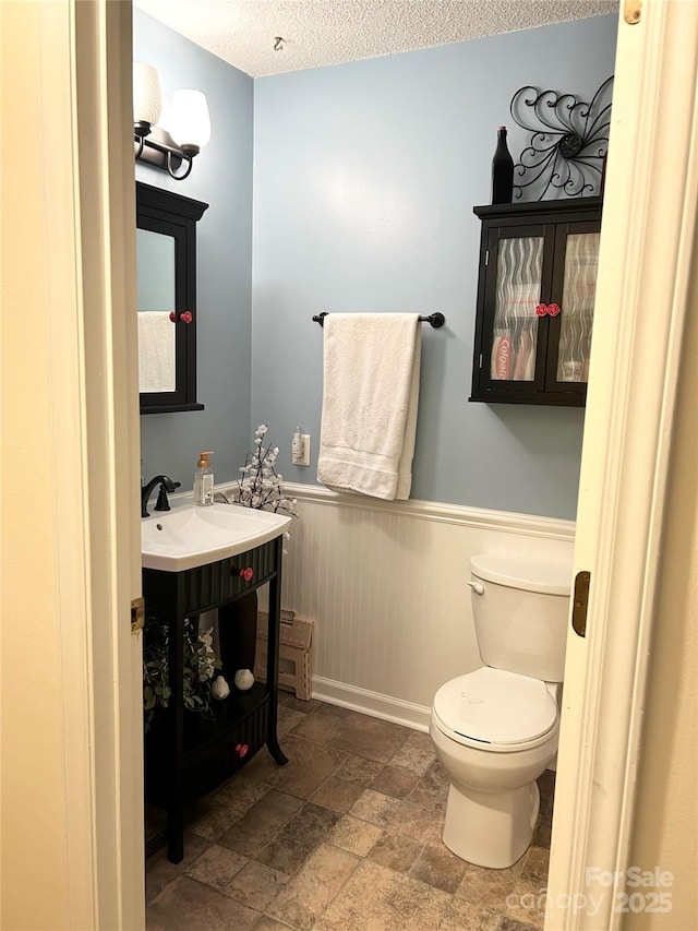 bathroom with vanity, toilet, a textured ceiling, and wooden walls