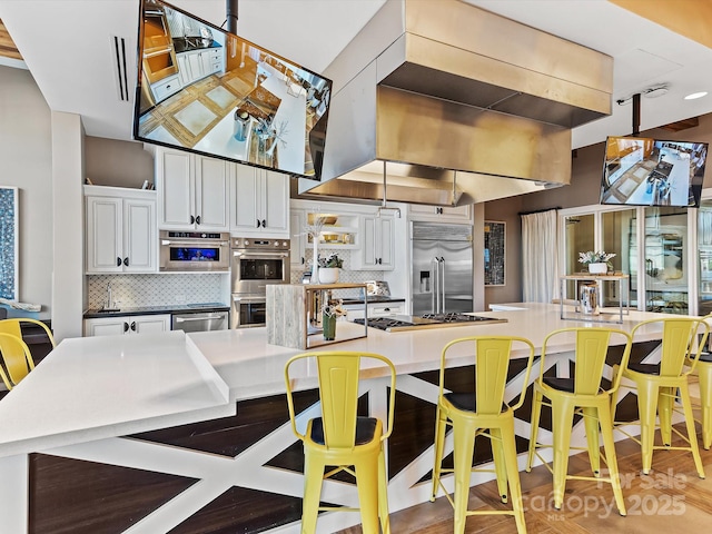 kitchen with a breakfast bar area, decorative backsplash, white cabinetry, and stainless steel appliances