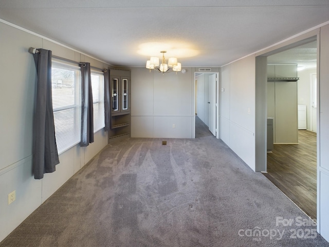 spare room featuring an inviting chandelier and dark colored carpet