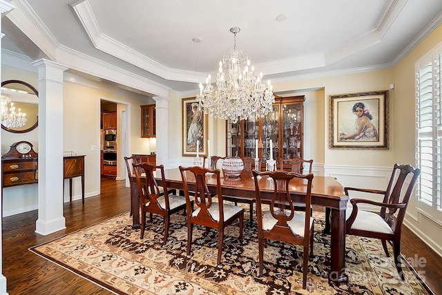 dining area featuring decorative columns, dark wood-type flooring, a raised ceiling, ornamental molding, and a chandelier