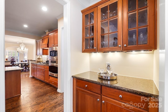 kitchen featuring dark stone counters, ornamental molding, appliances with stainless steel finishes, dark hardwood / wood-style flooring, and a chandelier