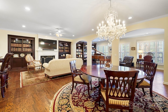 dining area featuring built in shelves, ceiling fan with notable chandelier, dark wood-type flooring, and ornamental molding