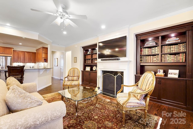 living room featuring ceiling fan, built in features, crown molding, and dark wood-type flooring