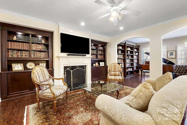 living room with built in shelves, ceiling fan, dark wood-type flooring, and ornamental molding